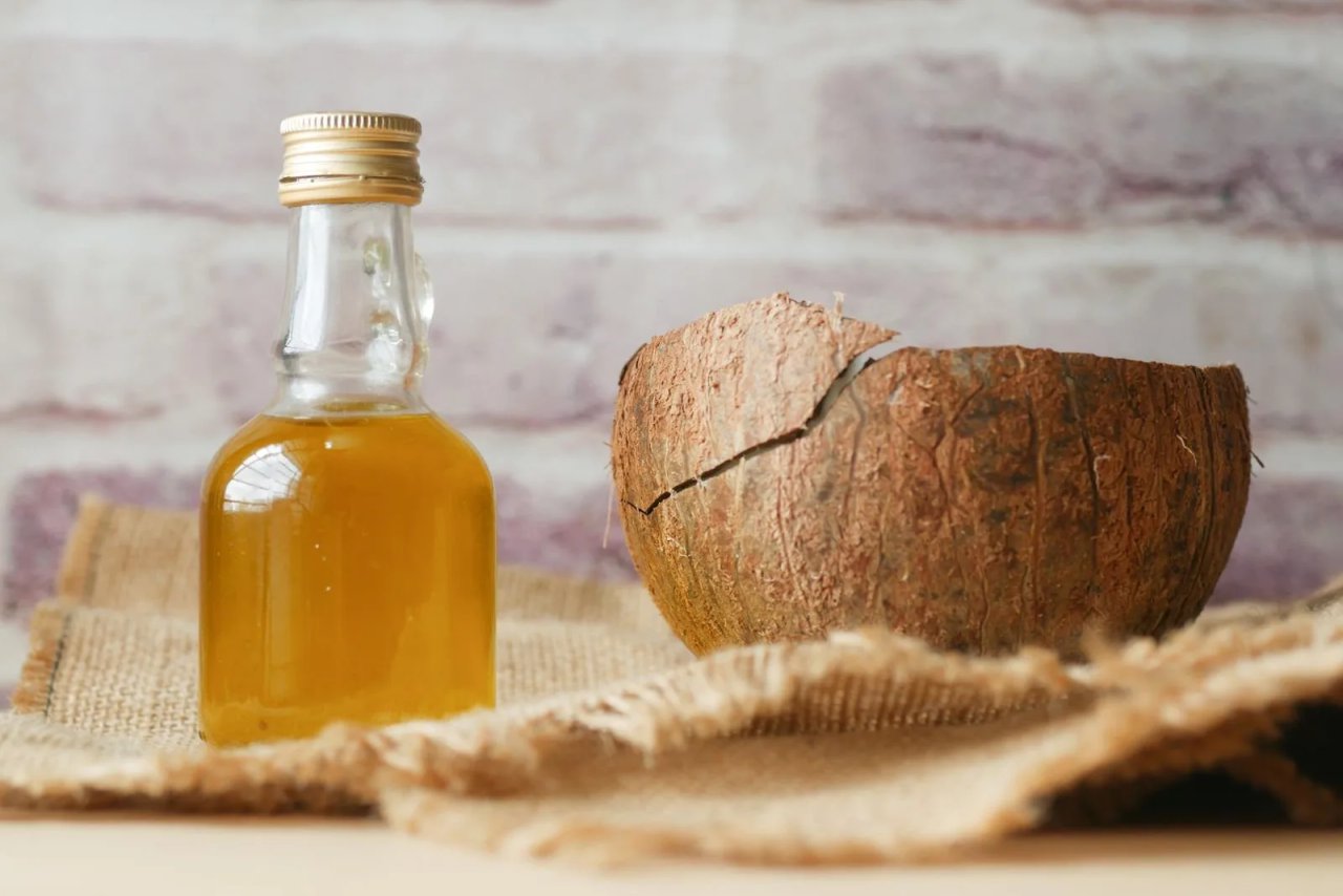 Glass bottle of coconut hair oil beside a coconut shell